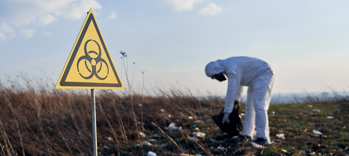 Hazardous waste being collected by someone in a protective suit and mask.